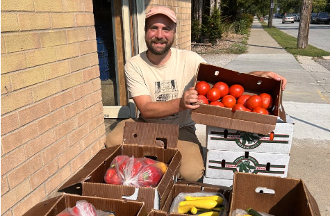  Will Moyer the Food Hub Manager at 阿格斯农场站 stands behind several boxes of produce